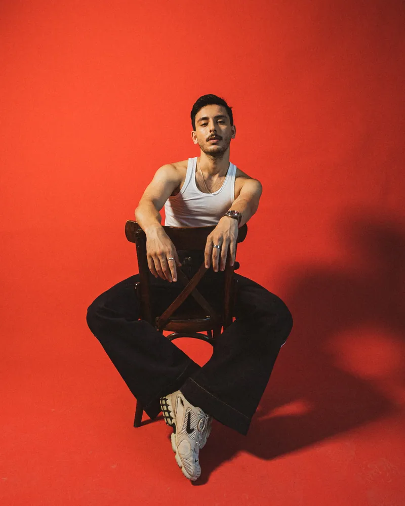 Hasan Raheem seated on a wooden chair against a red backdrop