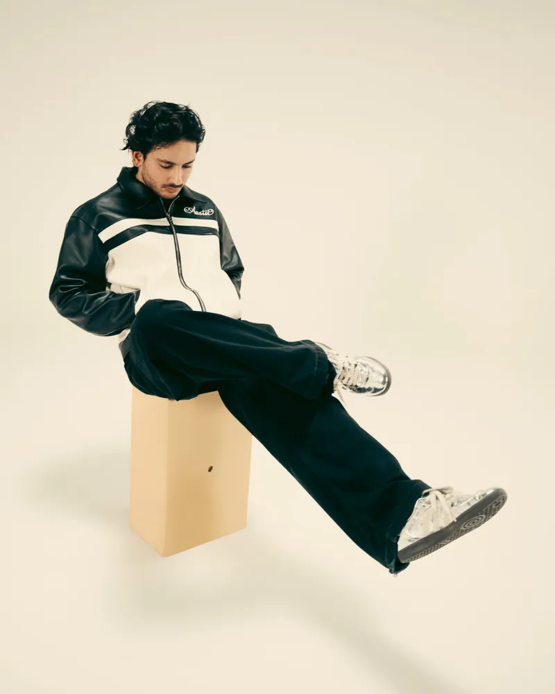 Hasan Raheem seated on a block in a studio, silver sneakers